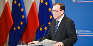 Mariusz Kaminski an einem Rednerpult, im Hintergrund Flaggen Polens und der EU