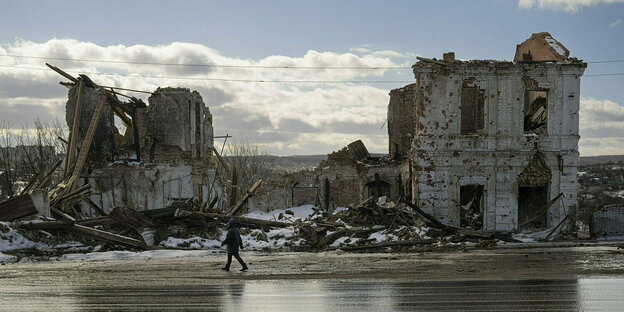A person walks past a ruined house