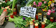 Blumen und ein SChild auf dem geschrieben steht "Trauer und Wut über das fehlende Waffenverbot"
