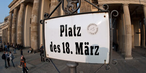 Ein weißes Schild mit der Aufschrift "Platz des 18. März" vor dem Brandenburger Tor in Berlin