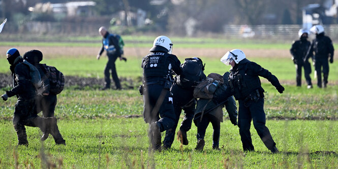 Behelmte Polizisten ringen mit Klimaaktivisten auf einem Feld