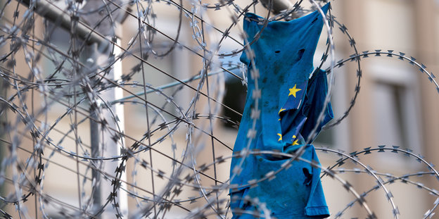 Eine zerrissene Europaflagge hängt in einem Stacheldrahtzaun