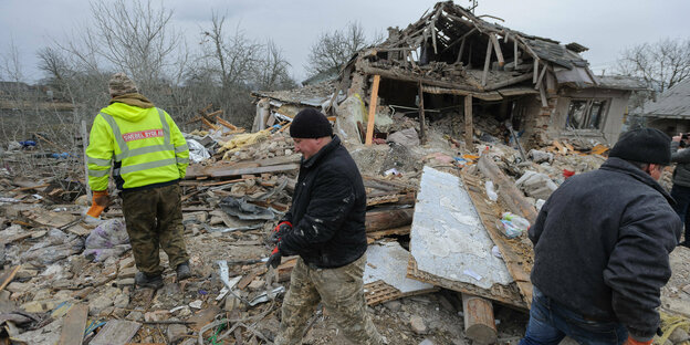 Several men walk through the remains of a collapsed house