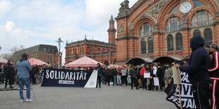 Vor dem Haupotbahnhof in Bremen stehen Menschen, auf einem Transparent steht: Solidariät statt Polizei