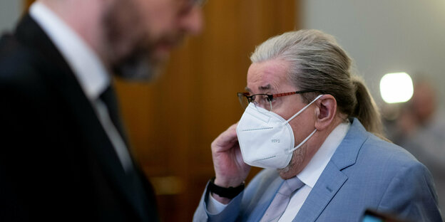 Man in a suit wears a mask and talks on the phone in the courtroom.