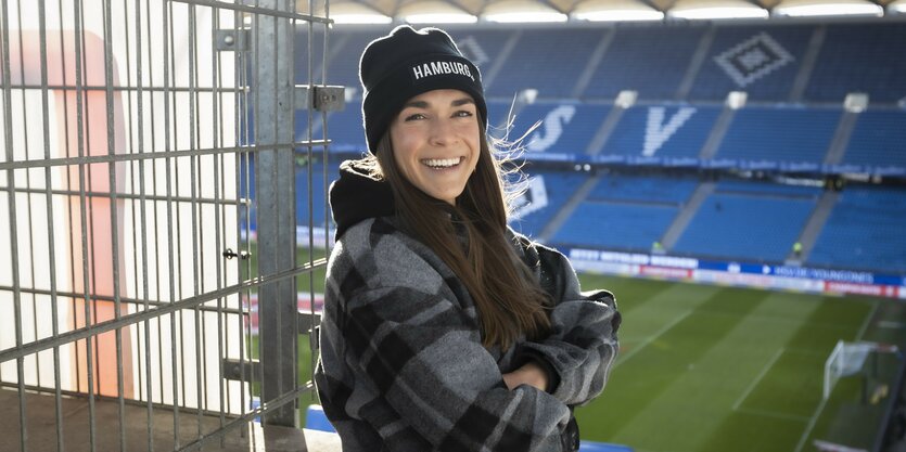 Eine junge Frau mit einer schwarzen Mütze, auf der "Hamburg" steht, steht auf der Tribühne im HSV-Stadion