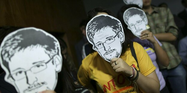 Das Bild zeigt eine Gruppe von Menschen die Masken von Edward Snowden tragen