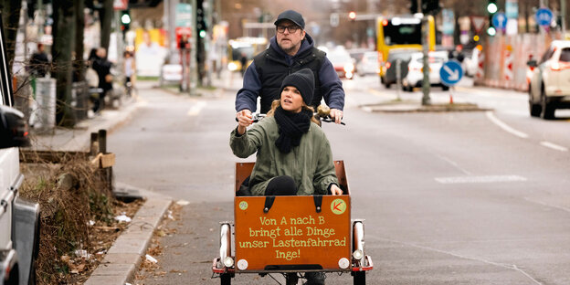 Die Schauspieler*innen Anke Engelke und Bjarne Mädel fahren auf einem Lastenrad durch Hamburg.