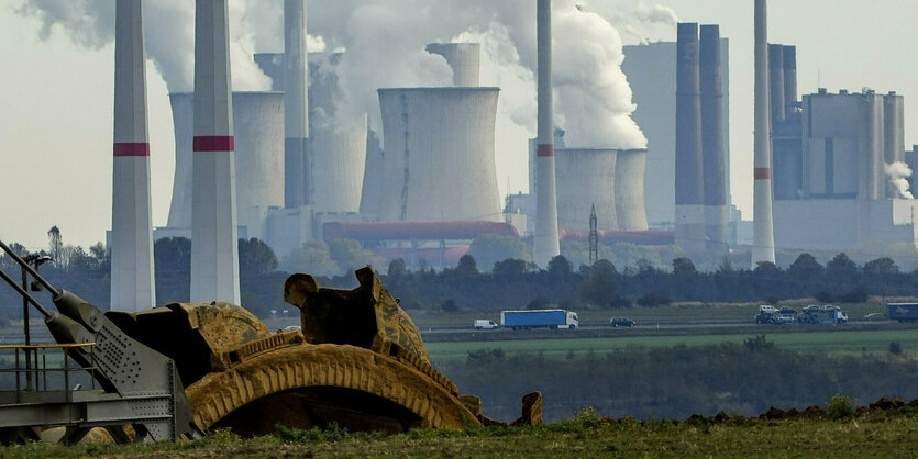 Kohlekraftwerk Neurath mit qualmenden Schloten, im Vordergrund ist ein Teil eines Schaufelbaggers des Braunkohleabbaus zu sehen