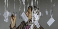 Eine alte Frau mit Kopftuch liest Zettel mit Namen, die von der Decke hängen