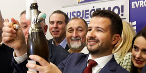 Der lächelnde Jakov Milatovic öffnet eine Flasche Sekt, umringt von Parteifreunden