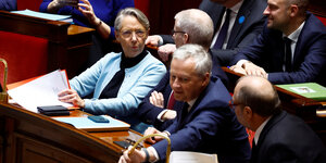 Premierministerin Elisabeth Borne sitzt neben zwei Kollegen in der Nationalversammlung und hört aufmerksam zu