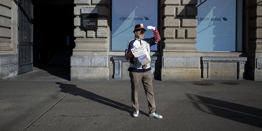 Ein Mann steht mit einem Schild in den Händen vor einer Bankfiliale und hält sich die Hand vor die Augen