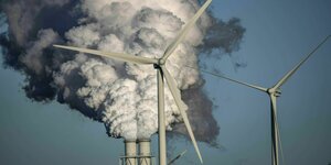 Die Rauchfahren eines RWE Kohlekraftwerks, davor stehen Windräder