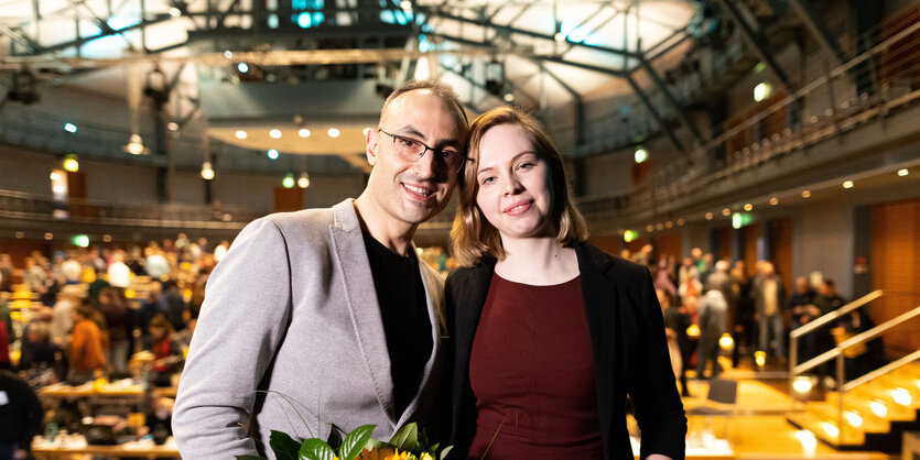 Die neuen Landesvorsitzenden der niedersächsischen Grünen, Alaa Alhamwi und Greta Garlichs, stehen nach ihrer Wahl in einer Halle und lächeln in die Kamera.