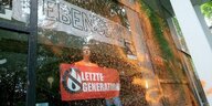 Besprühte Fensterfront des Hamburger Audimax, dahiner Aktivistin der Letzten Generation mit Transparent