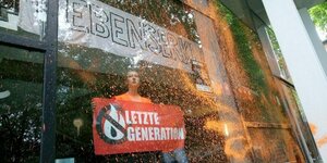 Besprühte Fensterfront des Hamburger Audimax, dahiner Aktivistin der Letzten Generation mit Transparent