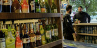 Alkoholflaschen stehen in einem Regal, 2 Männer unscharf im Hintergrund