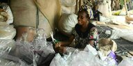 Müllsammlerin in Lagos sitzt zwischen Plasitiksäcken und hält eine Schere in der Hand