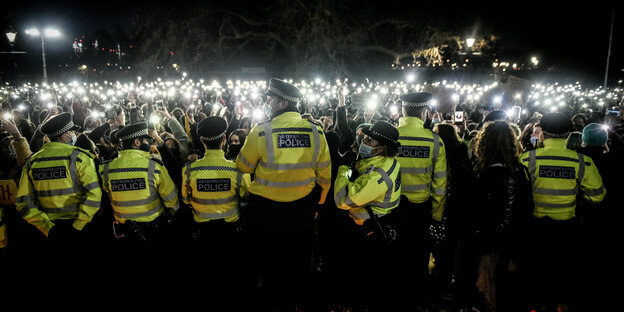 A wall of cell phone lights illuminates a police line seen from behind