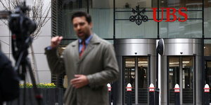 Ein Journalist steht vor einer Kamera und spricht vor der UBS in London in die Kamera