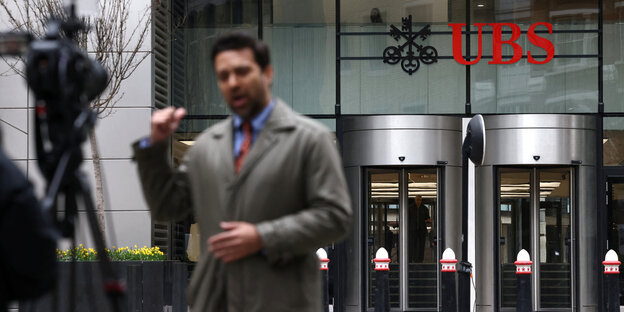 Ein Journalist steht vor einer Kamera und spricht vor der UBS in London in die Kamera