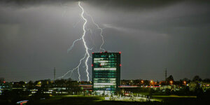 Hinter einem beleuchteten Bürokomplex in Esslingen schlägt ein Blitz ein