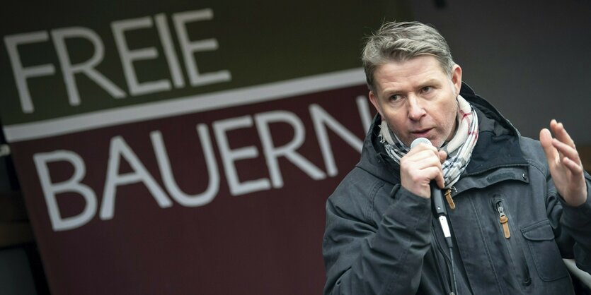 Ein Mann spricht bei einer Demo in ein Mikrofon. Hinter ihm hängt ein Transparent mit der Aufschrift "Freie Bauern".