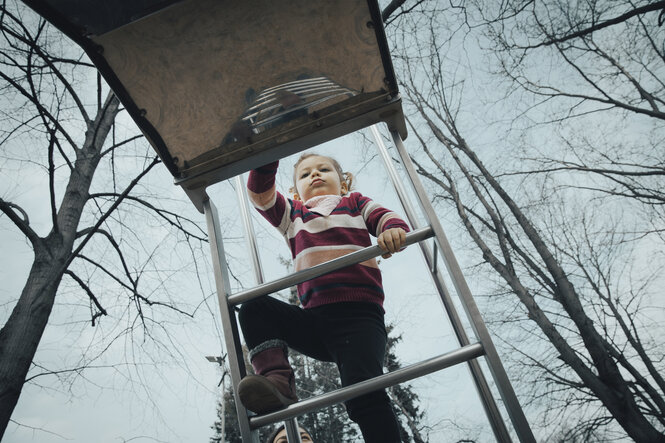 Ein zweijähriges Kind klettert die Leiter zu einer Spielplatz-Rutsche hinauf