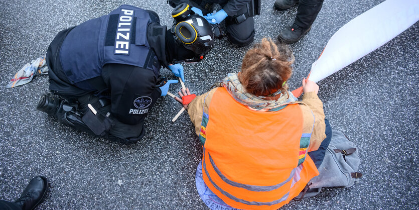 Polziste versucht, die angeklebt Hand einer Klimaaktivistin von der Straße zu lösen