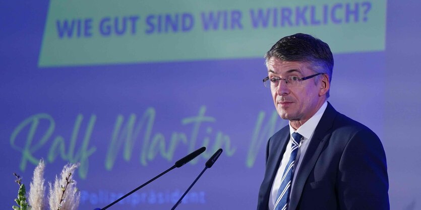 Polizeipräsident Ralf Martin Meyer an Mikrofonen vor einer violetten Wand auf der die Frage steht: "Wie gut sind wir wirklich?", darunter seine Unterschrift