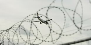 Stacheldraht. Im Hintergrund ein Flugzeug in der Luft