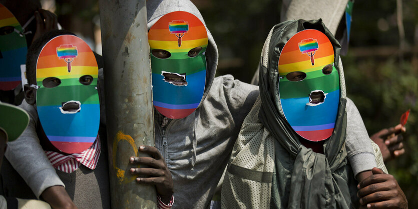 3 Männer stehen nebeneinander, sie haben sich Masken in Regenbogenfarben gemacht, Augen und Mund sind herausgeschnitten