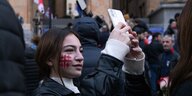 Eine Frau hat sie die georgische Fahne auf die Wange gemalt und fotografiert sich mit ihrem Handy