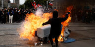 Ein Mann springt vor einer brennenden Mülltonnne