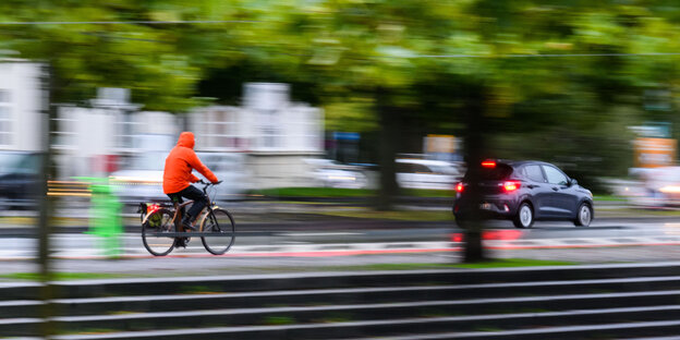 Ein Mann fährt mit einem Fahrrad am frühen Morgen neben einem Auto durch die Stadt