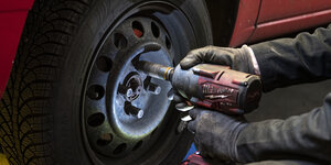 Ein Mechaniker schraubt den Reifen eines Autos ab.