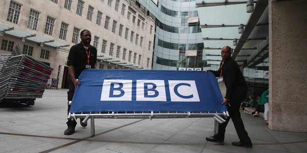 Zwei Männer tragen ein BBC-Schild