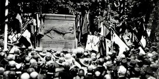 Menschen stehen bei einer Feier rund um ein steinernes, quaderförmiges Denkmal