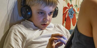 Ein Junge mit Kopfhörern starrt auf sein Smartphone