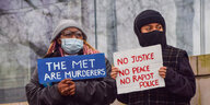 Zwei Demonstranten halten Plakate mit den Aufschriften The Met are murderers und No justice, no peace, no rapist police