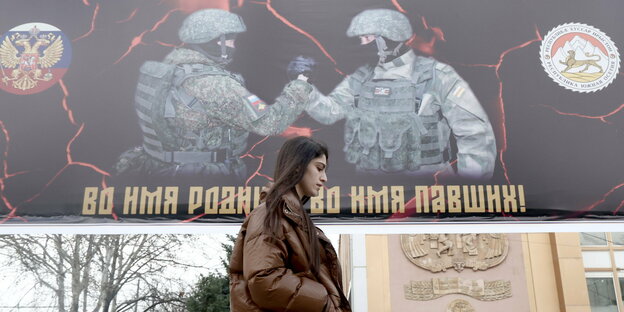 Eine Frau läuft vor einem Plakat worauf ein Russischer Soldat und ein Soldat aus Südossetien zu sehen ist