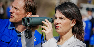 Außenministerin Baerbock hat einen Feldstecher und steht an der Verwaltungslinie zu Südossetien am Beobachtungspunkt Nummer 5 bei Odzisi mit Sebastian Hulde, einem EUMM-Mitabeiter.