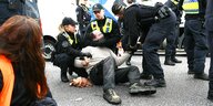 Mehrere Polizisten umklammern einen auf der Straße liegenden Mann, um ihn von der Fahrbahn zu entfernen