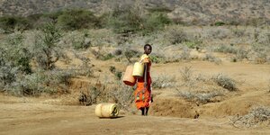 Frau mit wasserkanistern in einer trockenen Gegend