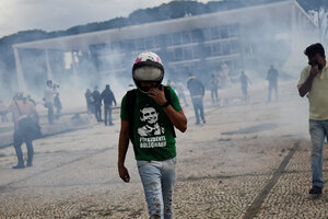 Ein Mann in Bolsonaro-Shirt und Jeans läuft über einen verrauchten Platz. Er trägt einen Helm.