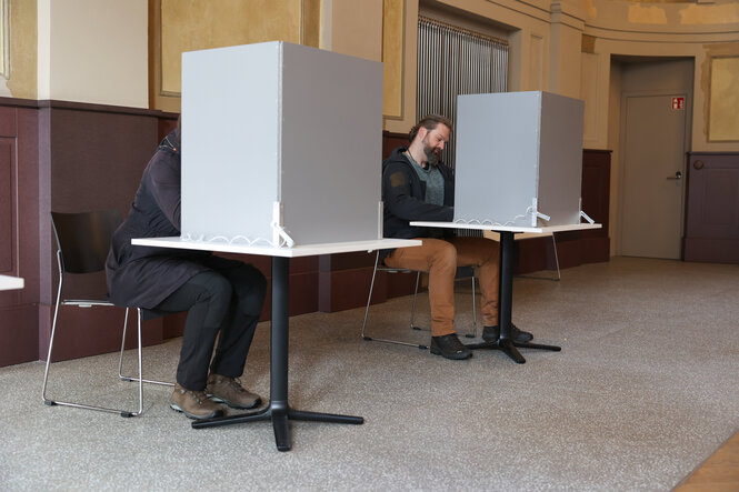 Menschen sitzen in zwei Wahlkabinen