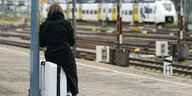 Eine Frau sitzt auf ihrem Rollkoffer auf einem Bahnsteig und wartet