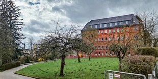 Ein mehrstöckiges rotes Bachsteingebäude, davor eine grüne Wiese mit Obstbaum ohne Blätter