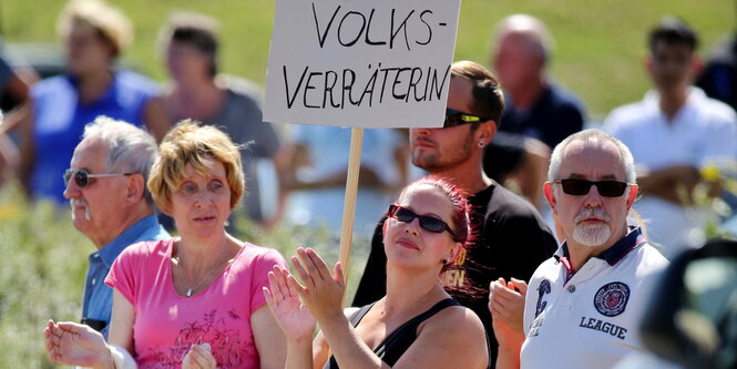 Menschen klatschen und halten ein Schild „Volksverräterin“